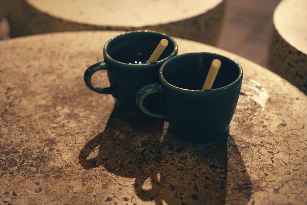 Deux tasses de café posées sur une table en pierre sous un éclairage chaleureux.