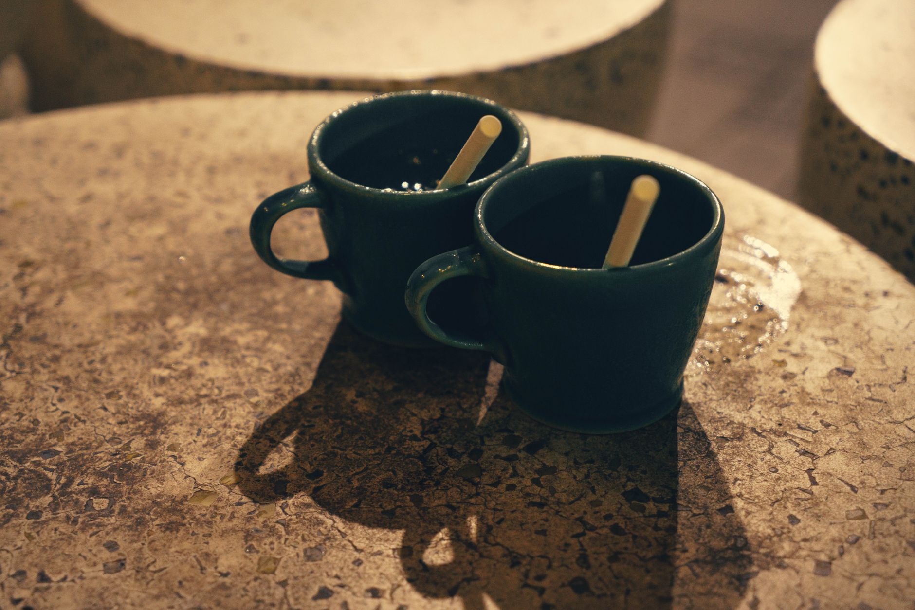 Deux tasses de café posées sur une table en pierre sous un éclairage chaleureux.