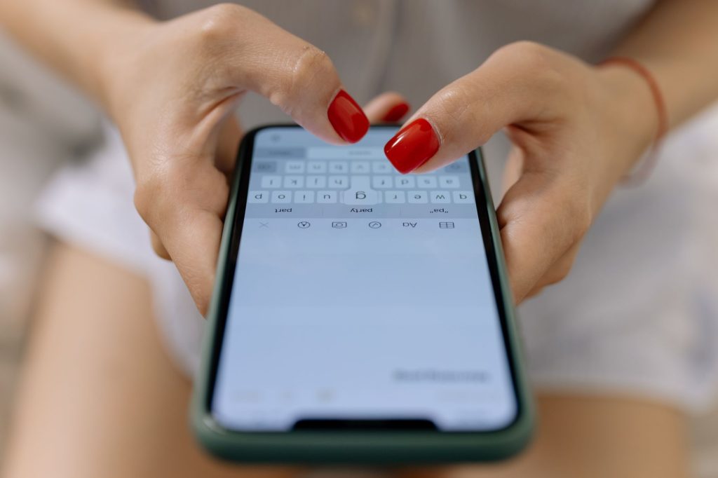 Gros plan sur les mains d'une femme aux ongles rouges tapant un message sur l'écran de son smartphone.