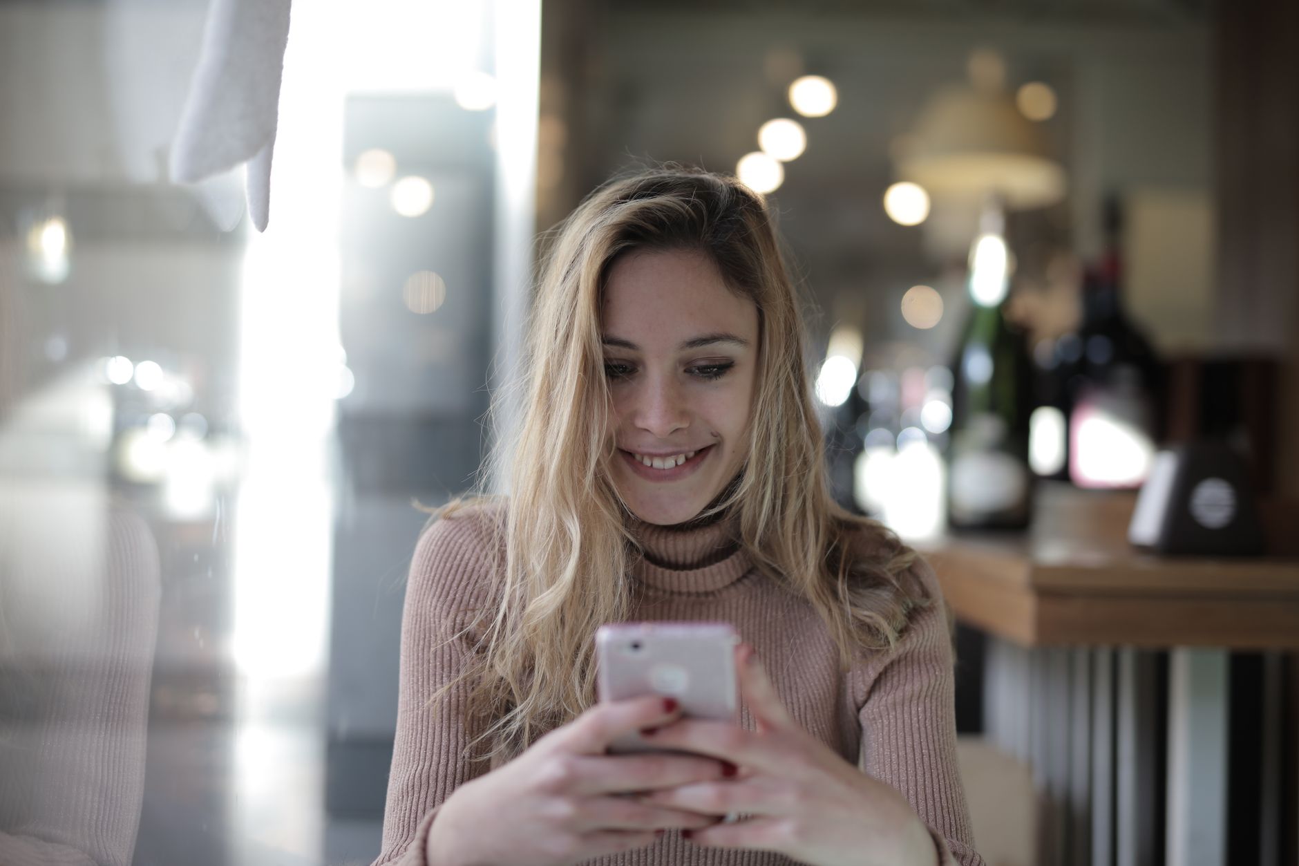 Une jeune femme sourit en écrivant un message sur son smartphone.