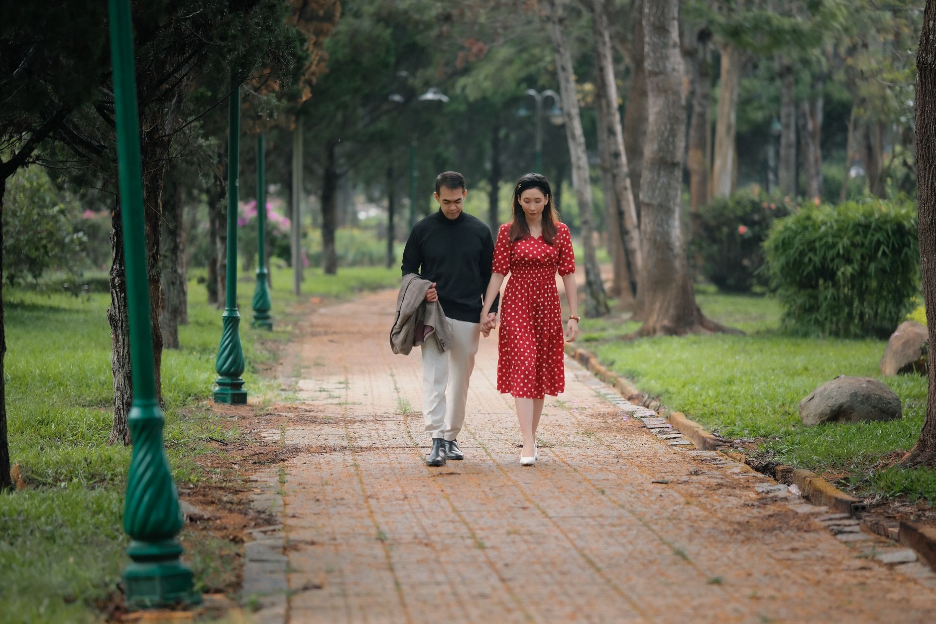 Un couple marche main dans la main sur une allée pavée dans un parc arboré.
