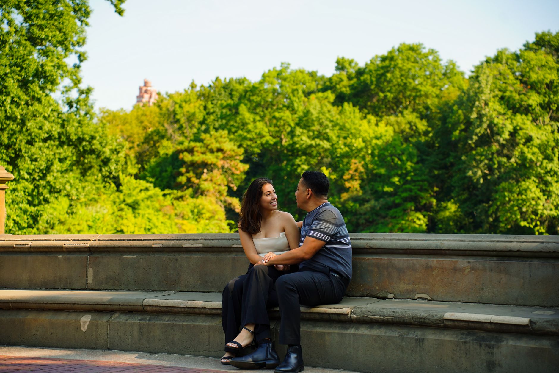Un couple assis sur un banc de pierre dans un parc, en pleine conversation.