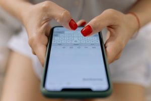 Gros plan sur les mains d'une femme aux ongles rouges en train de taper un message sur son smartphone.