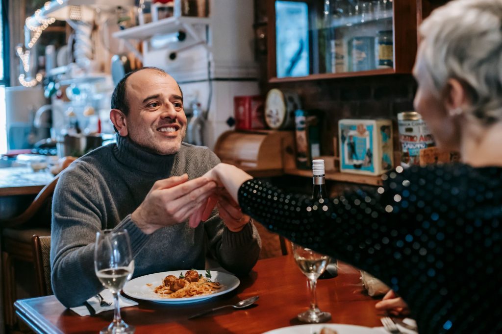 Un homme et une femme se tiennent la main en souriant lors d’un dîner au restaurant.