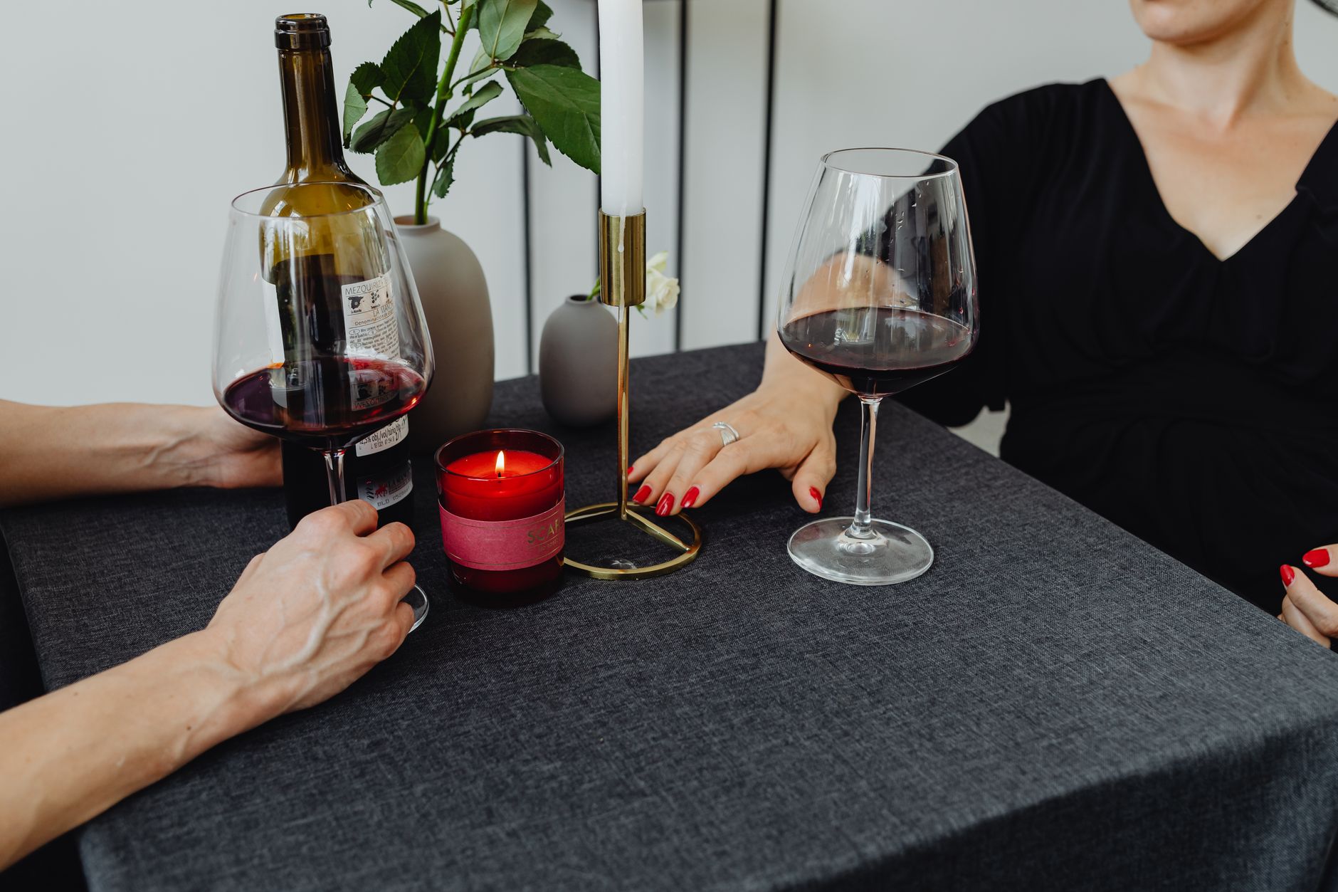 Un couple partageant un dîner romantique avec du vin rouge et des bougies sur une table nappée de gris.