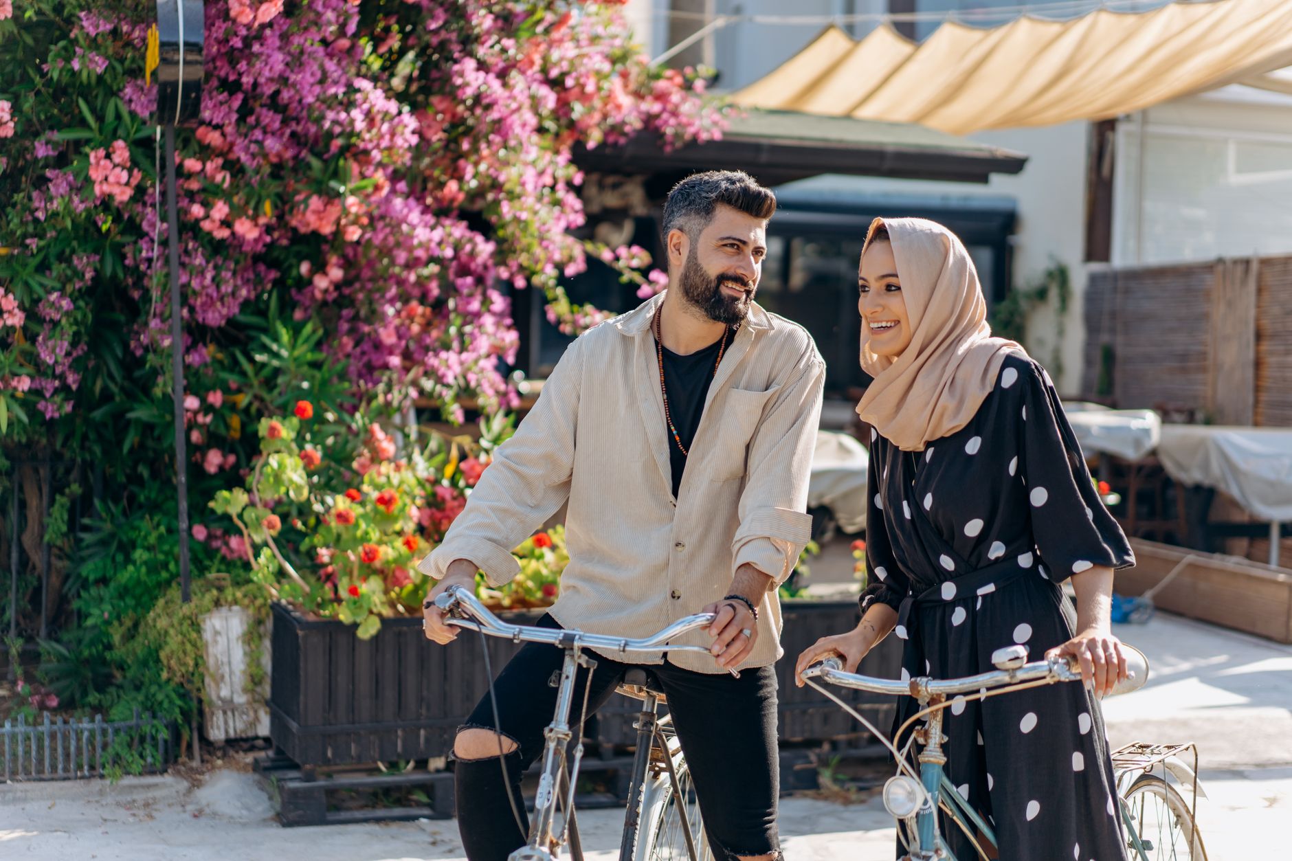 Un couple souriant se déplaçant à vélo dans une rue fleurie.